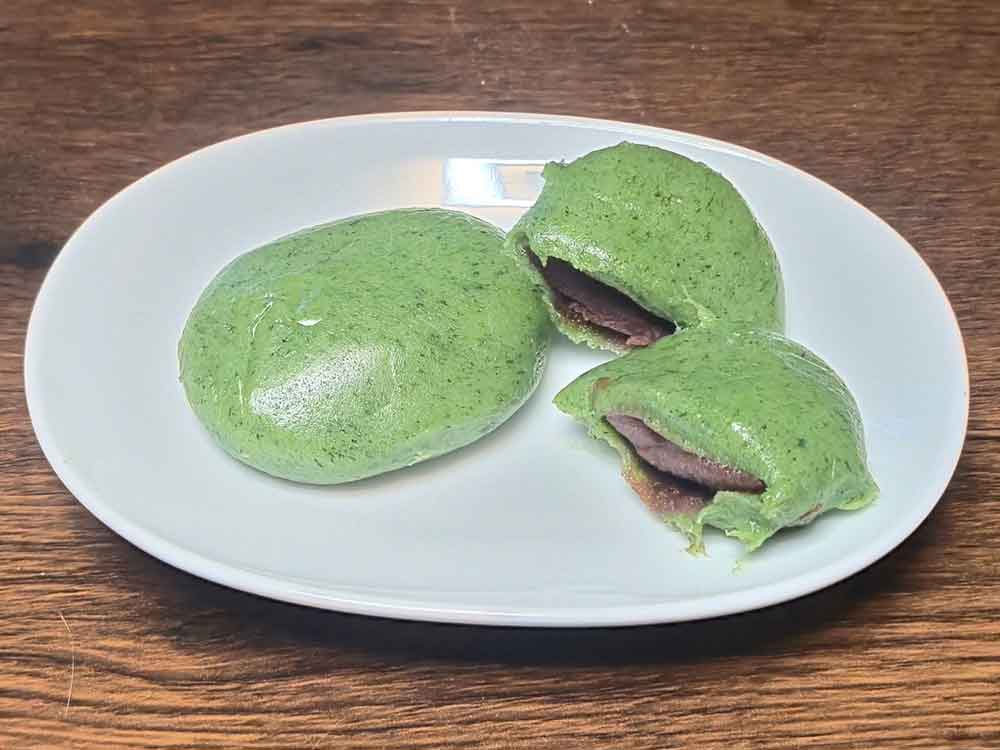 志満ん草餅の草餅（あん入り）。よもぎ餅の中に、なめらかで上品な甘さの餡がたっぷり入っている断面